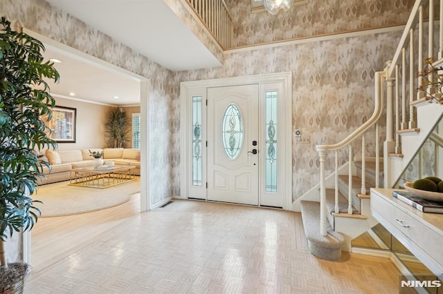 foyer featuring visible vents, stairway, a high ceiling, ornamental molding, and baseboards