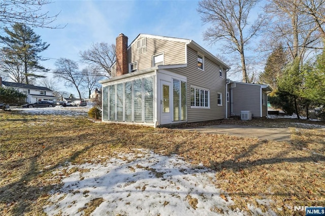 view of snowy exterior with a sunroom, a chimney, and central AC