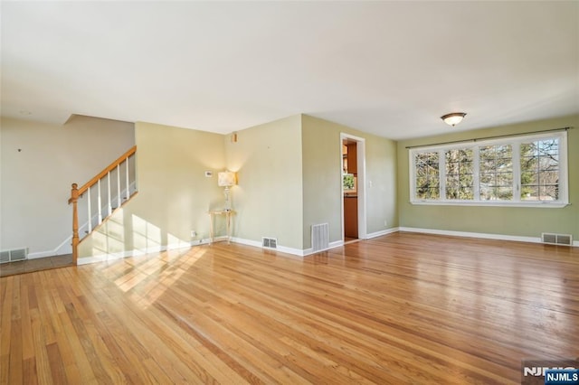 unfurnished living room featuring stairs, visible vents, and wood finished floors