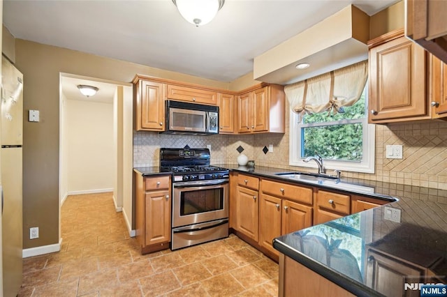 kitchen with stainless steel appliances, dark countertops, a sink, and tasteful backsplash