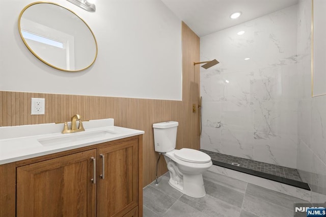 full bath featuring a wainscoted wall, a marble finish shower, recessed lighting, toilet, and vanity