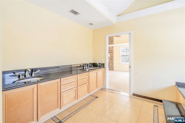 kitchen with light brown cabinetry, dark countertops, a sink, and visible vents