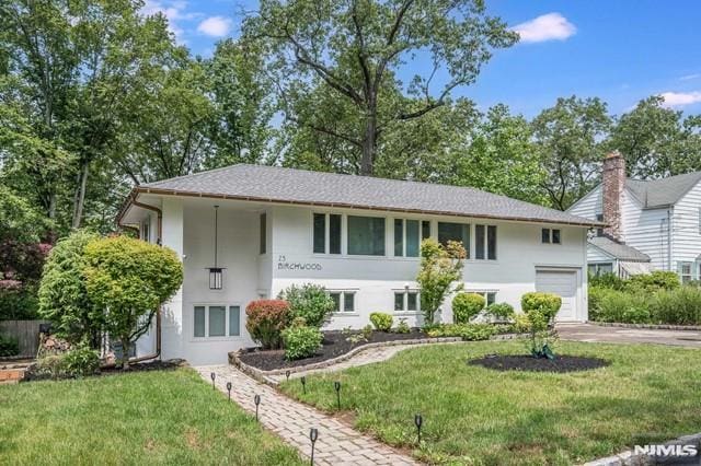 raised ranch with stucco siding, driveway, a garage, and a front yard