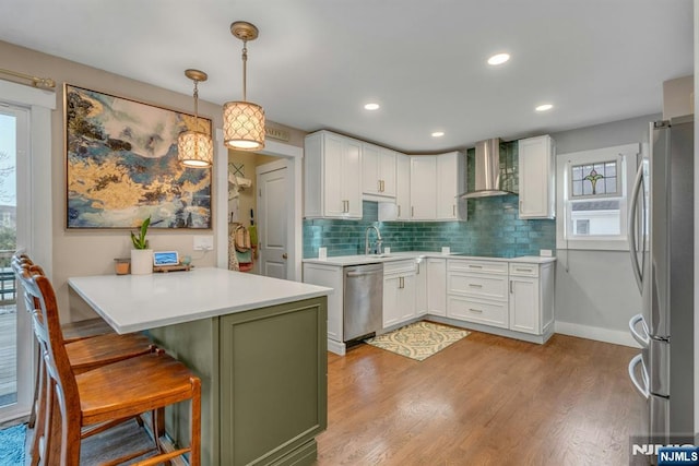 kitchen with stainless steel appliances, white cabinetry, a kitchen breakfast bar, wall chimney exhaust hood, and pendant lighting