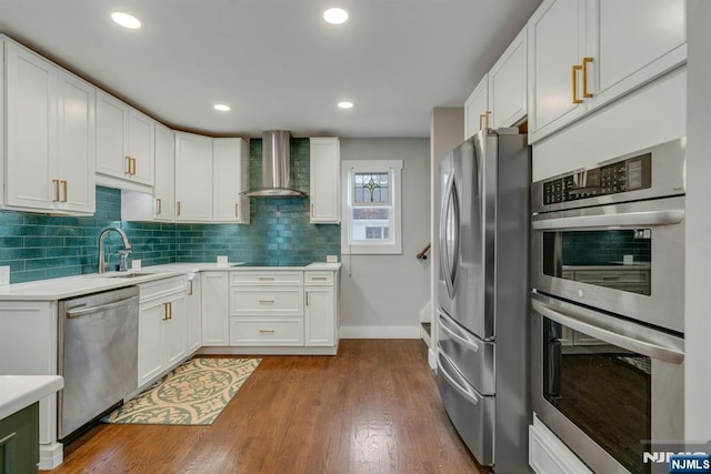 kitchen featuring light countertops, appliances with stainless steel finishes, white cabinetry, a sink, and wall chimney exhaust hood