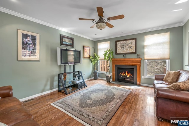 living area with baseboards, visible vents, a glass covered fireplace, hardwood / wood-style flooring, and ornamental molding