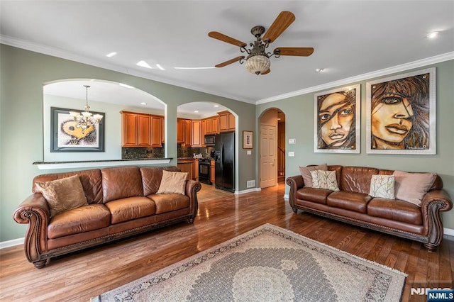 living room with arched walkways, baseboards, light wood-style flooring, ornamental molding, and ceiling fan with notable chandelier