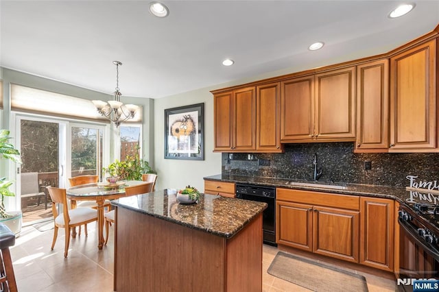 kitchen featuring a sink, a kitchen island, hanging light fixtures, black appliances, and dark stone countertops