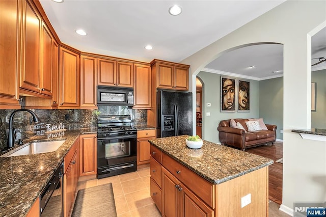 kitchen featuring open floor plan, a sink, a kitchen island, dark stone counters, and black appliances