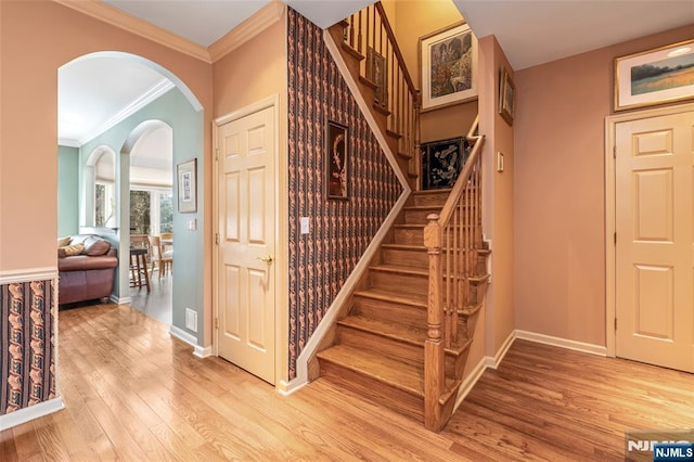 stairs featuring baseboards, arched walkways, wood finished floors, and crown molding