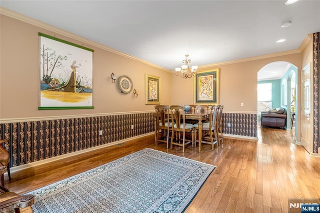 dining area featuring arched walkways, a wainscoted wall, light wood-style flooring, ornamental molding, and a chandelier