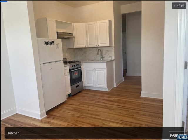 kitchen with freestanding refrigerator, white cabinetry, a sink, stainless steel gas range, and under cabinet range hood