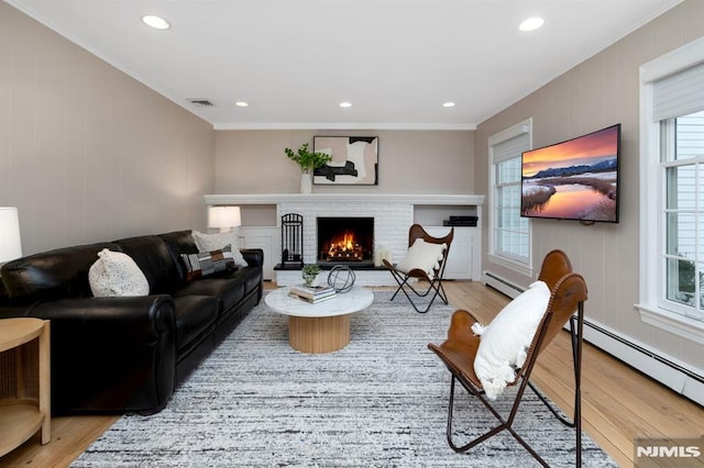 living room with a baseboard radiator, a brick fireplace, visible vents, and wood finished floors