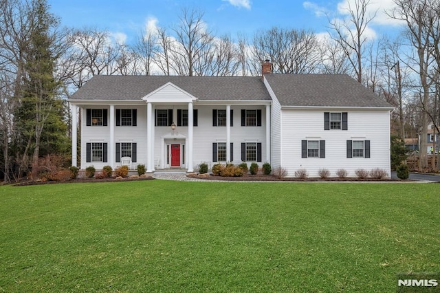 neoclassical / greek revival house featuring a front yard, roof with shingles, and a chimney