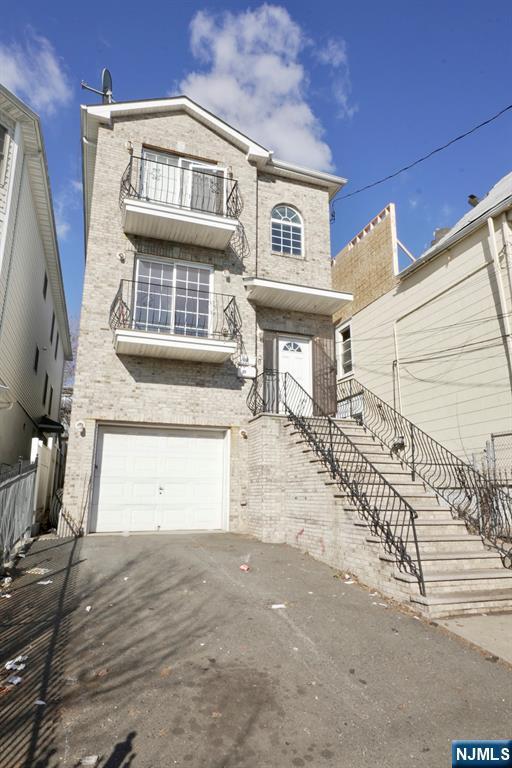 view of front of home featuring driveway, a balcony, an attached garage, fence, and brick siding