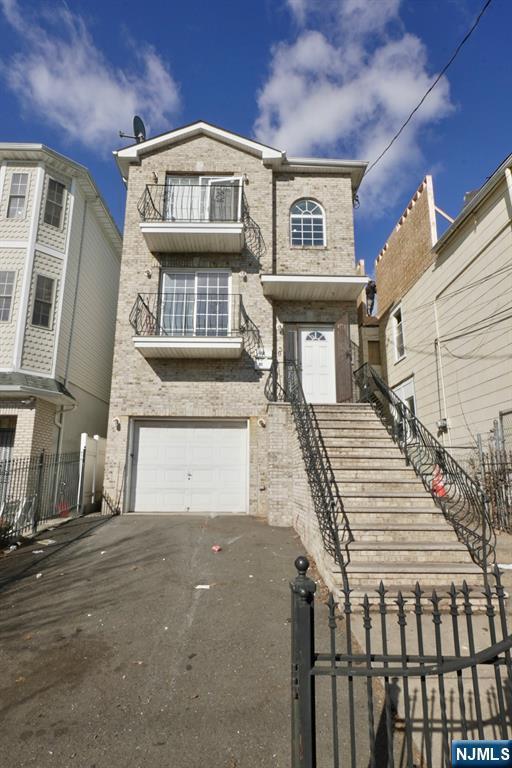 view of front of home featuring an attached garage, a balcony, brick siding, fence, and driveway