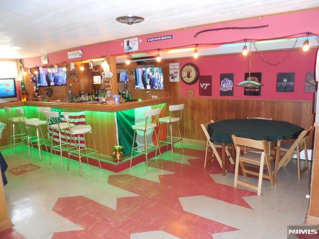 bar with wainscoting, wood walls, a bar, and tile patterned floors