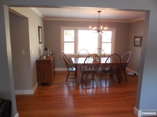 dining space featuring baseboards, ornamental molding, light wood-style flooring, and an inviting chandelier