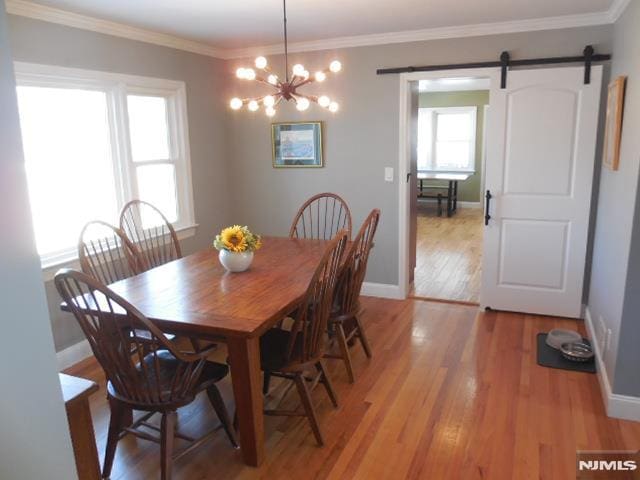 dining space with ornamental molding, a barn door, baseboards, and light wood-style floors