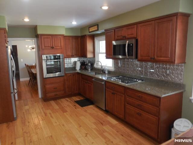 kitchen with tasteful backsplash, appliances with stainless steel finishes, light wood-style floors, brown cabinetry, and a sink