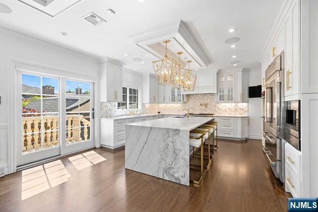 kitchen featuring a kitchen island with sink, glass insert cabinets, visible vents, and ornamental molding