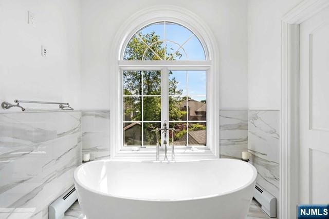 bathroom with tile walls, a soaking tub, and a baseboard radiator