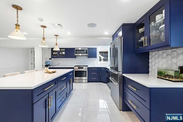 kitchen with light tile patterned floors, appliances with stainless steel finishes, pendant lighting, and blue cabinets