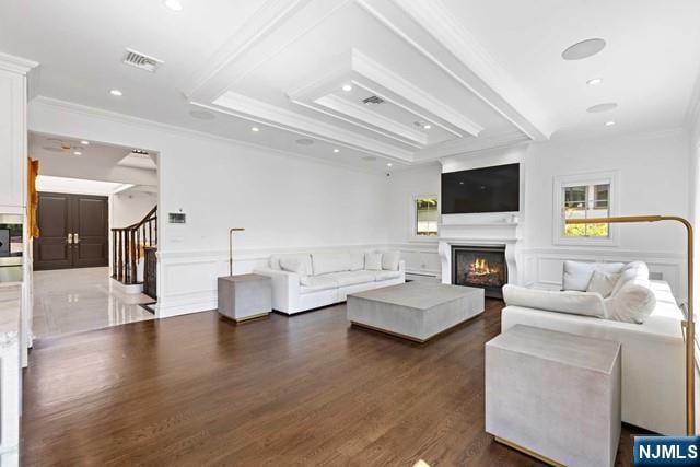 living room with a lit fireplace, stairs, crown molding, a raised ceiling, and a decorative wall