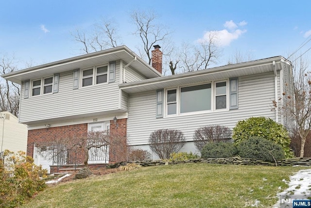 split level home featuring brick siding, a chimney, and a front yard