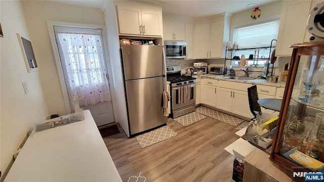 kitchen with stainless steel appliances, white cabinets, a sink, and light wood finished floors