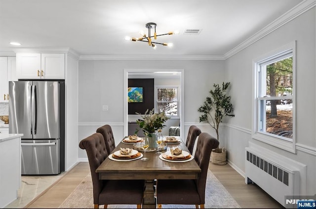 dining space with radiator, visible vents, light wood-style flooring, ornamental molding, and a chandelier