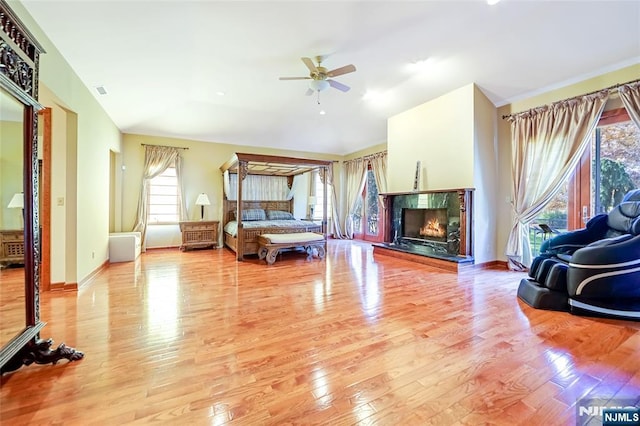 bedroom with light wood-style flooring, a ceiling fan, baseboards, and a premium fireplace