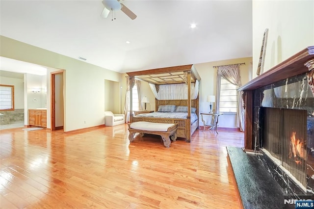 bedroom featuring lofted ceiling, multiple windows, a fireplace, and light wood-type flooring