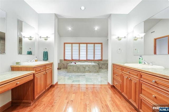 full bath featuring lofted ceiling, two vanities, wood finished floors, a bath, and a sink