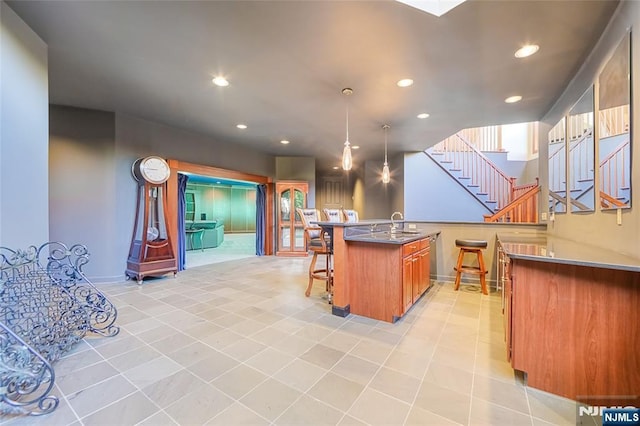 kitchen featuring a center island with sink, recessed lighting, hanging light fixtures, a kitchen breakfast bar, and brown cabinets