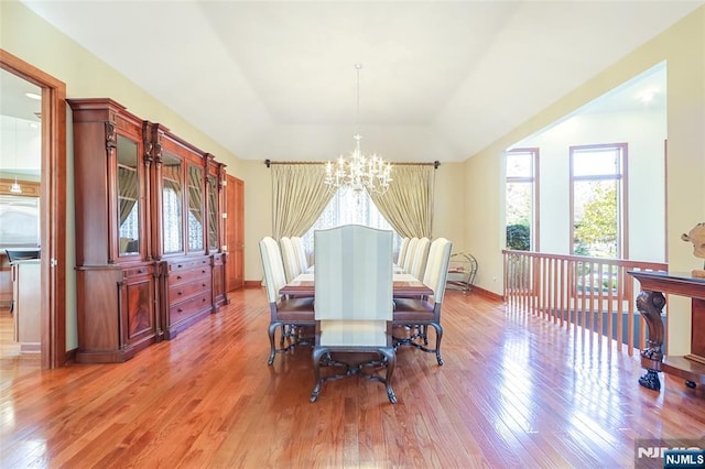 dining area featuring a raised ceiling, a notable chandelier, light wood-style floors, and a healthy amount of sunlight