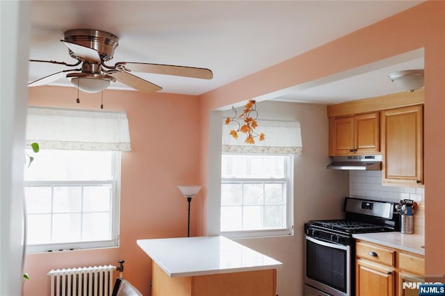 kitchen with tasteful backsplash, radiator, light countertops, under cabinet range hood, and stainless steel range with gas cooktop