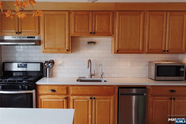 kitchen with brown cabinets, stainless steel appliances, light countertops, a sink, and under cabinet range hood