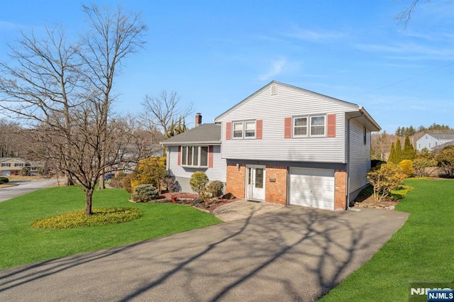 split level home featuring aphalt driveway, brick siding, a chimney, and a front lawn