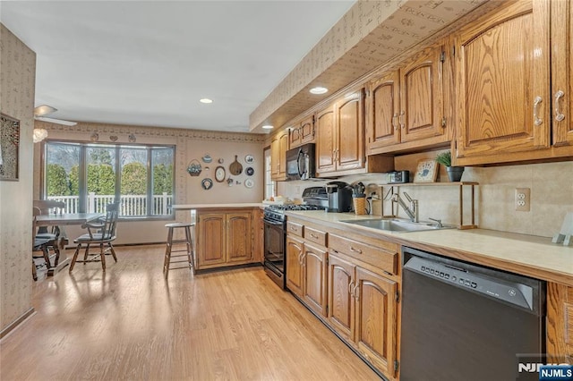 kitchen featuring light wood-style flooring, a peninsula, light countertops, black appliances, and a sink