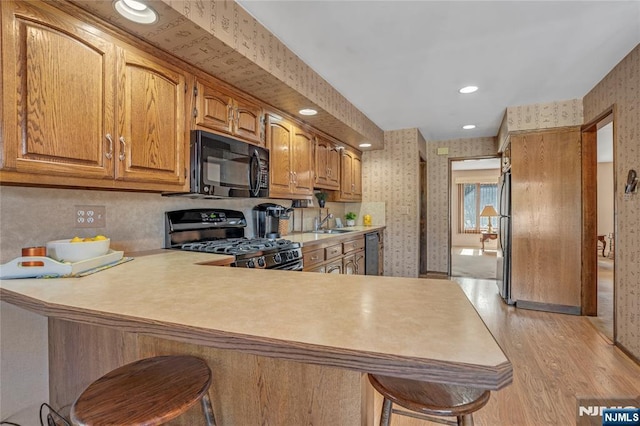 kitchen with black microwave, a sink, gas range, and wallpapered walls