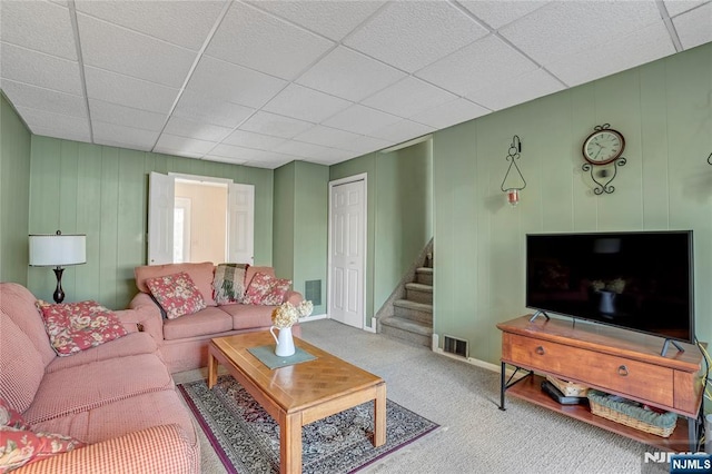 carpeted living area with baseboards, stairs, visible vents, and a drop ceiling