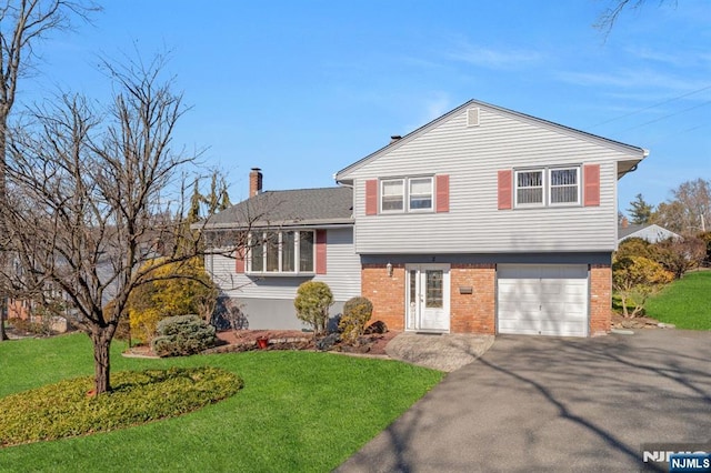 tri-level home with driveway, a garage, a chimney, a front lawn, and brick siding