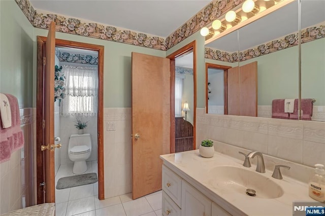 bathroom featuring a wainscoted wall, tile walls, toilet, vanity, and tile patterned floors