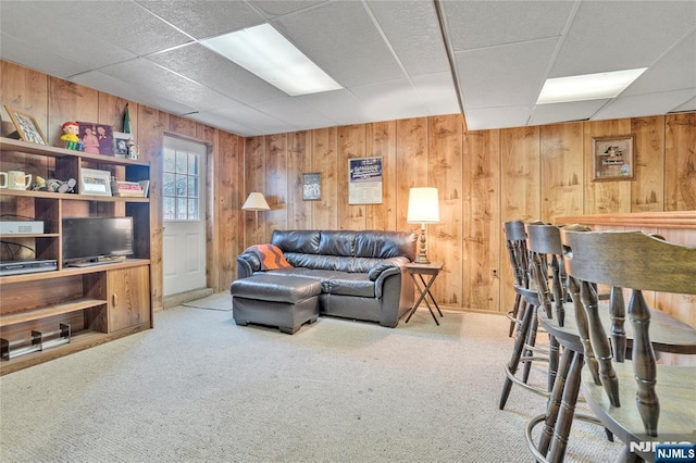 carpeted living room featuring a drop ceiling and wood walls