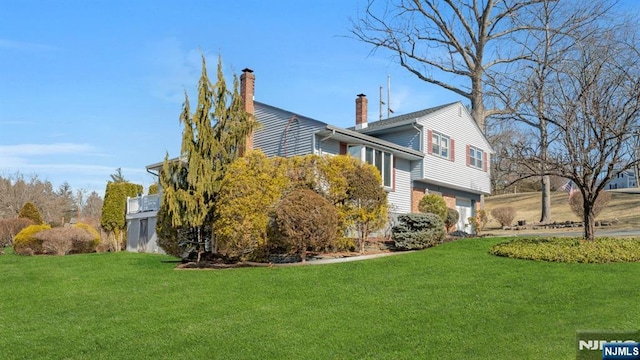 view of side of home with an attached garage, a chimney, and a yard