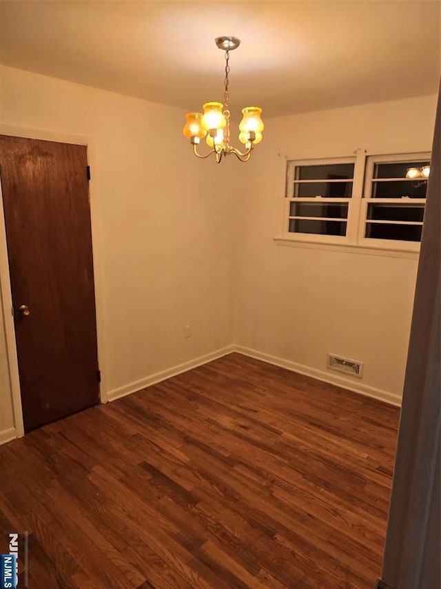 empty room featuring baseboards, visible vents, dark wood finished floors, and a chandelier