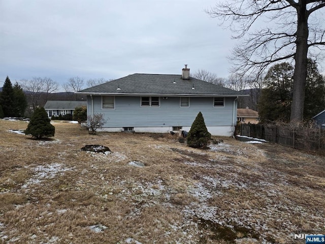 back of house featuring a shingled roof, a chimney, and fence