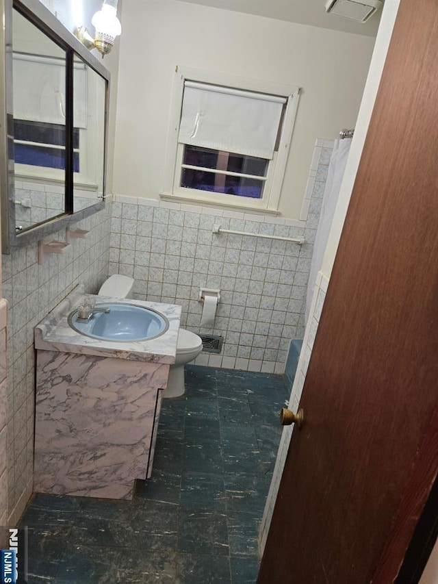 full bath featuring tile patterned flooring, toilet, a wainscoted wall, vanity, and tile walls