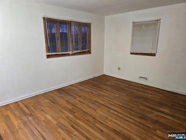 spare room featuring dark wood-style flooring, visible vents, and baseboards